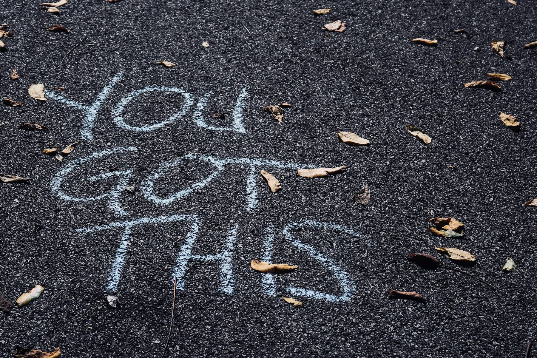 The words “you got this” chalked on asphalt scattered with autumn leaves